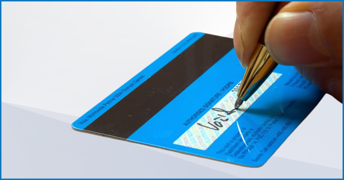 A hand signing the back of a credit card